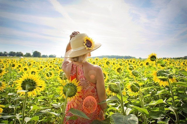 tu-campo-de-influencia Mujer de espaldas, mirando al horizonte en un campo de girasoles mientras se sujeta el gorro con una mano