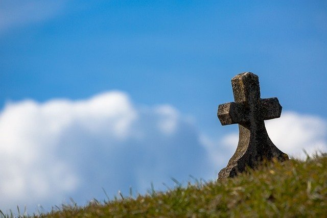 Cruz de una lápida que surge desde el césped y con el cielo de fondo
