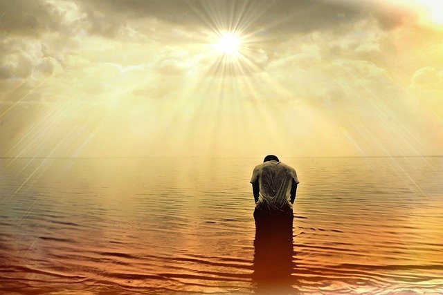 Persona de espaldas, bañándose en el mar a contraluz, y con el sol brillando en el centro